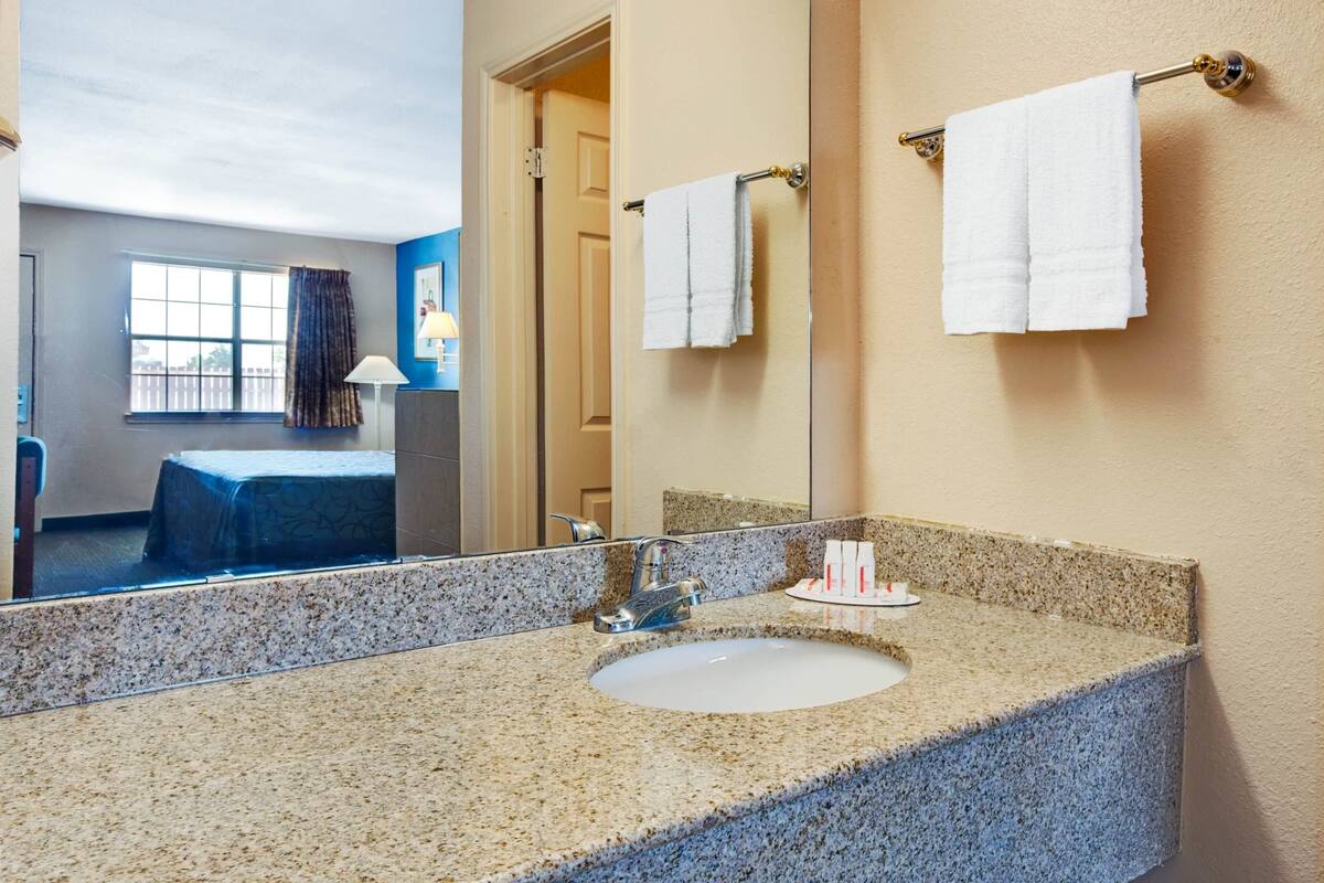 A hotel bathroom with a granite countertop sink, a large mirror, and two towels hanging on a towel rack.