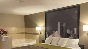A hotel room with a bed, a cityscape mural on the wall, a bathtub, and a vanity with a mirror. - Super 8 by Wyndham Terrell (Terrell)