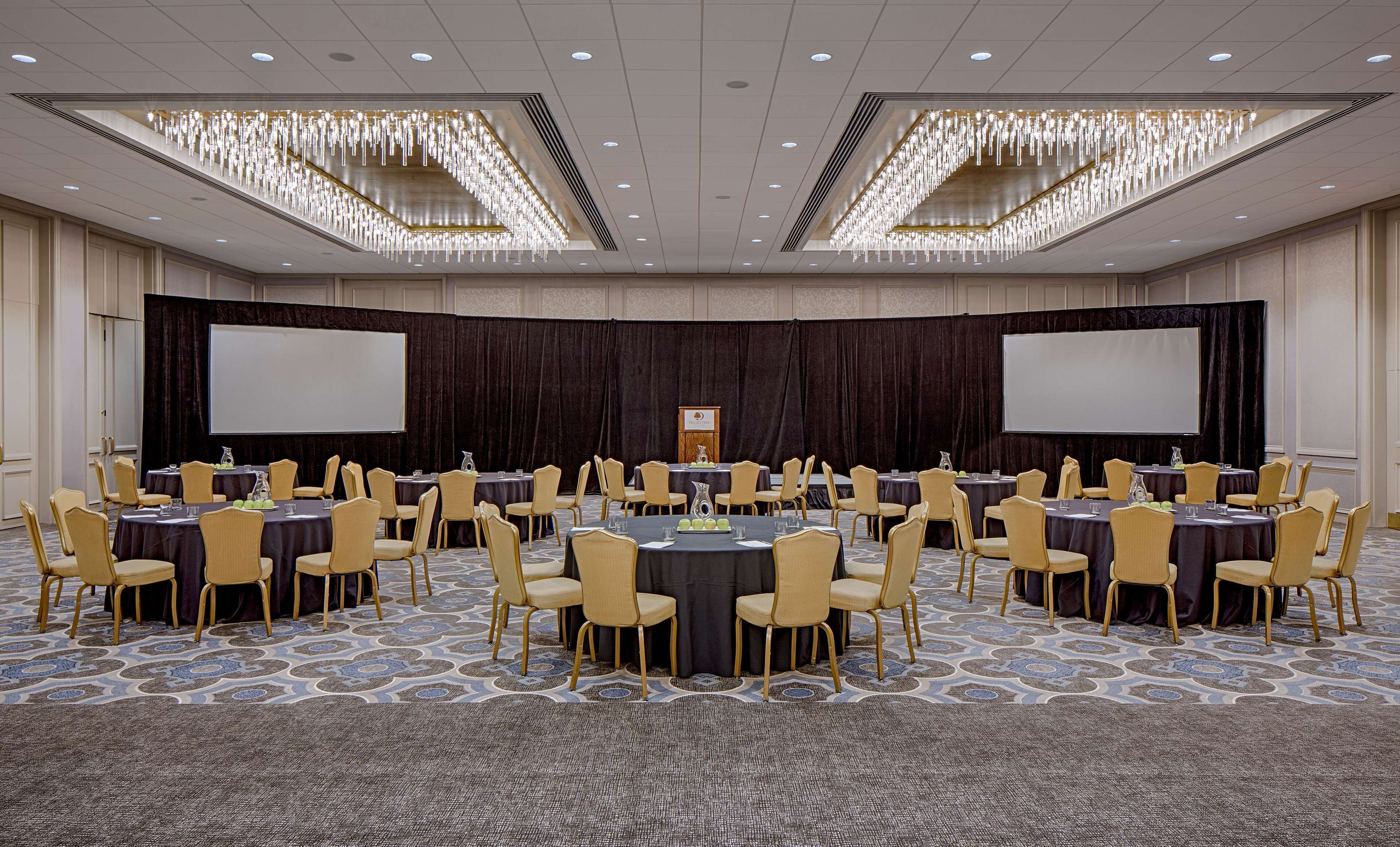 A conference room with round tables and chairs, a large screen, and a podium.
