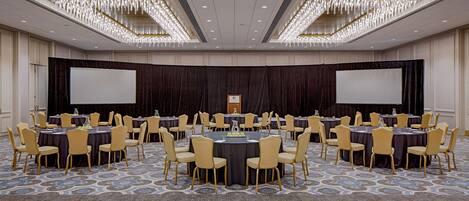 A conference room with round tables and chairs, a large screen, and a podium.