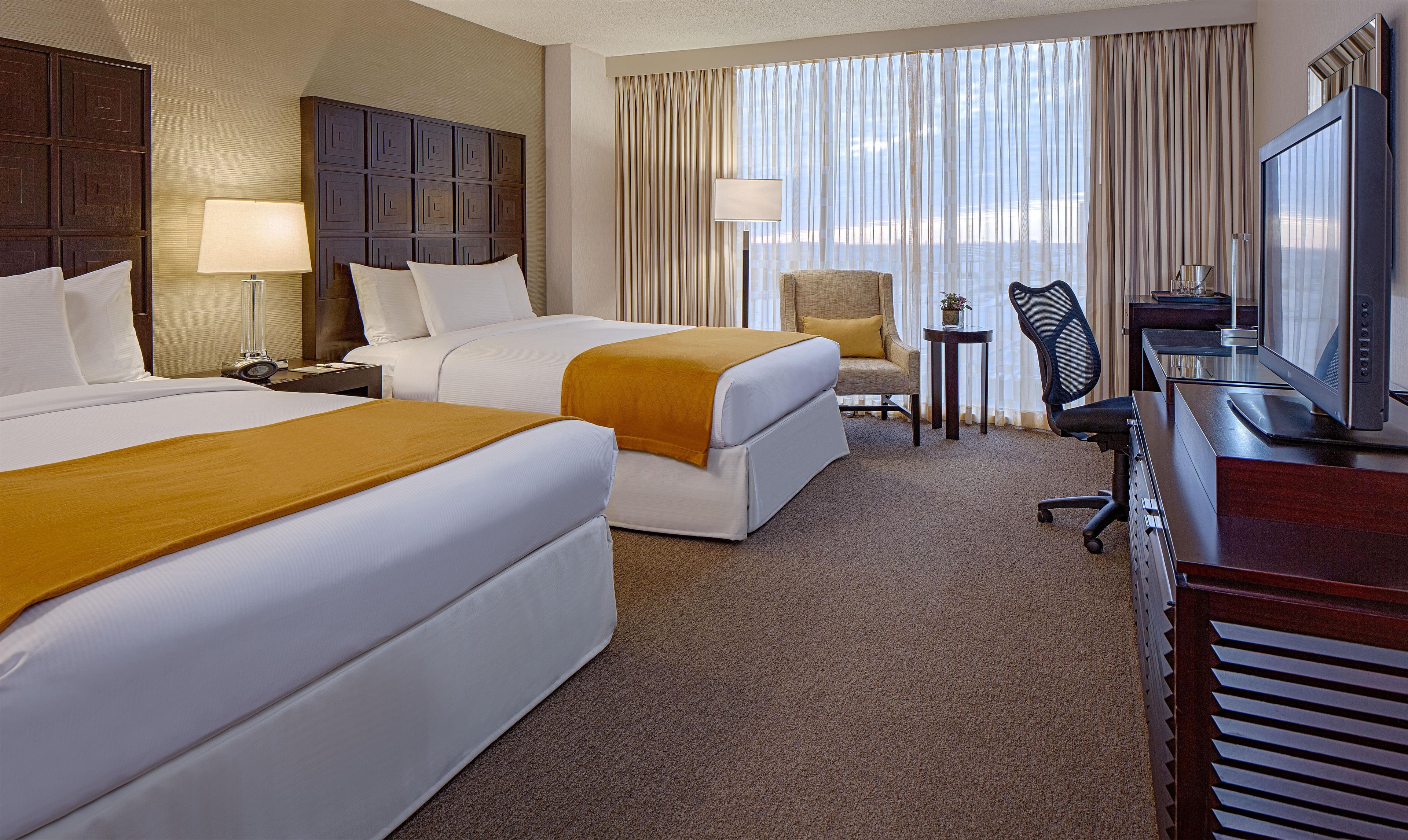 A hotel room with two beds, a desk with a computer, a chair, and a window with curtains.