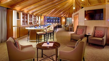 A hotel lobby with a bar area, seating arrangements, and a large TV screen.