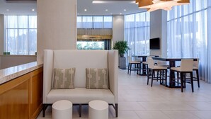 A modern hotel lobby with a sofa, dining area, and large windows. - DoubleTree by Hilton Hotel Houston - Greenway Plaza (Houston)