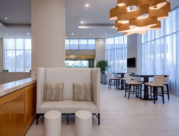 A modern hotel lobby with a sofa, dining area, and large windows.