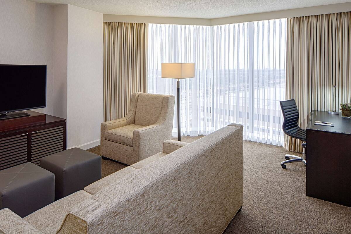 Une chambre d’hôtel équipée d’un téléviseur à écran plat, d’un canapé, d’un fauteuil, d’un bureau et d’une lampe.