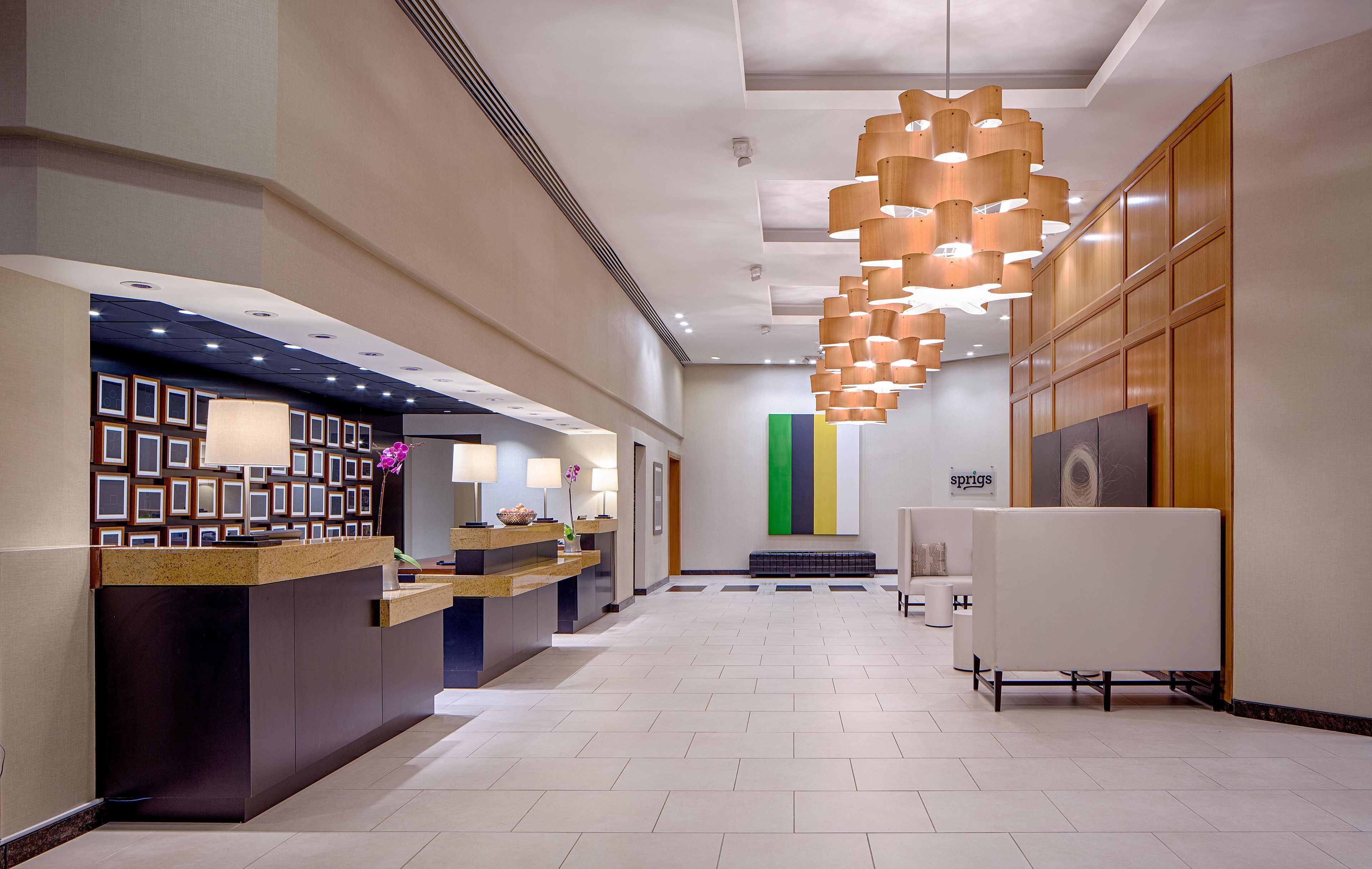 A hotel reception area with a reception desk, a seating area with a bench, and a modern light fixture.