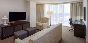 Habitación de hotel con televisor de pantalla plana, un sofá, una silla, un escritorio y una lámpara.