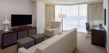 A hotel room with a flat-screen TV, a sofa, a chair, a desk, and a lamp.