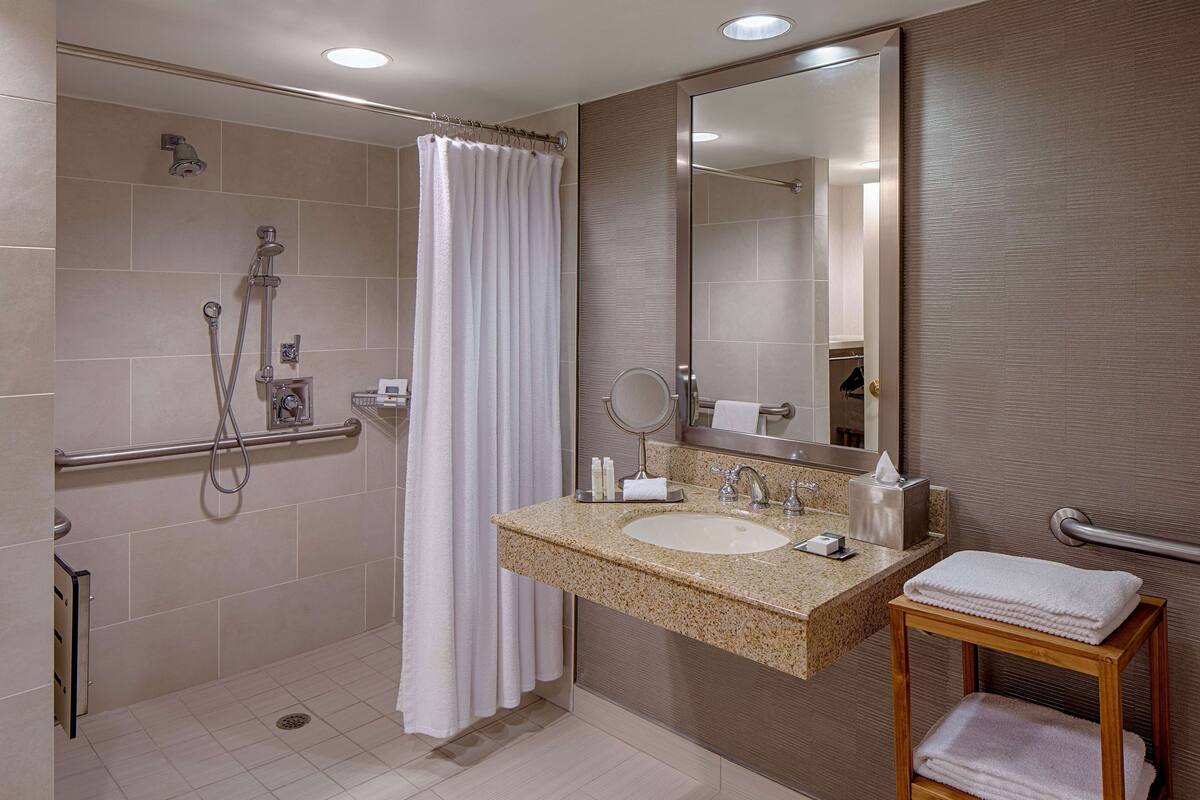 Une salle de bain moderne équipée d’une douche, d’un lavabo, d’un miroir et d’un porte-serviettes.