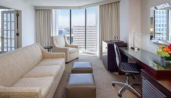 Quarto de hotel com sofá, poltrona, escrivaninha e vista para a paisagem urbana.