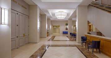 A hotel lobby with a reception desk, seating area, and a staircase.