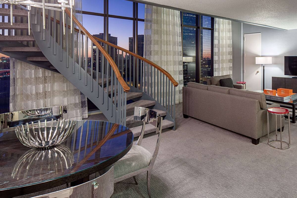 Un salon moderne avec une table en verre, un canapé, un téléviseur et un escalier offrant une vue sur la ville.