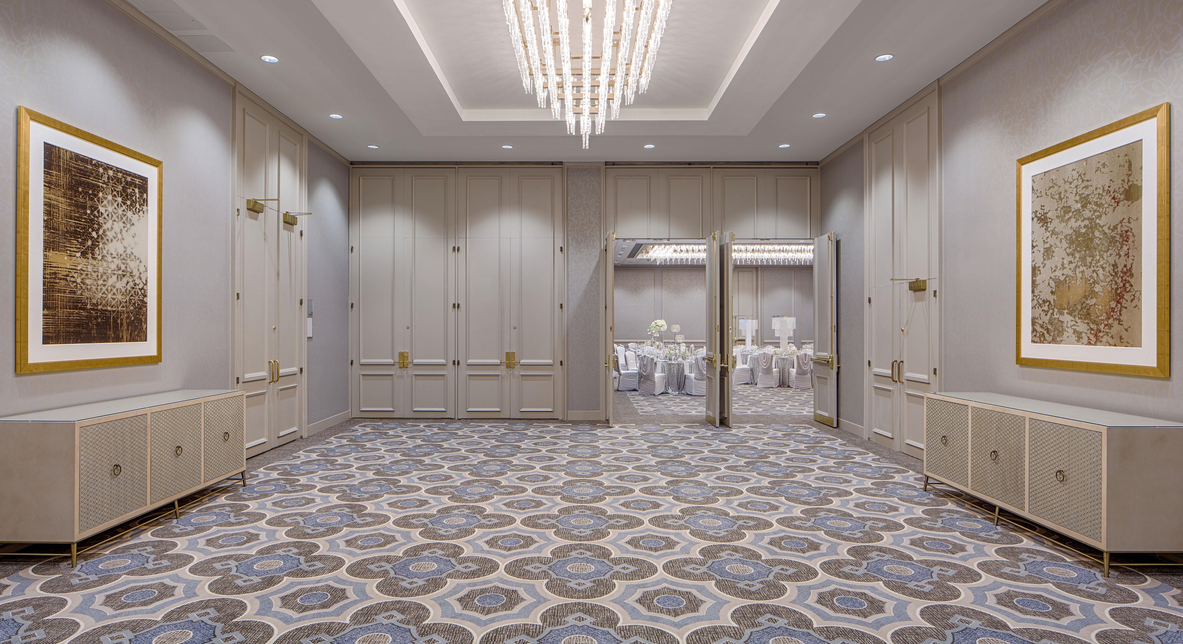 A spacious room with a patterned floor, large doors, and a chandelier.