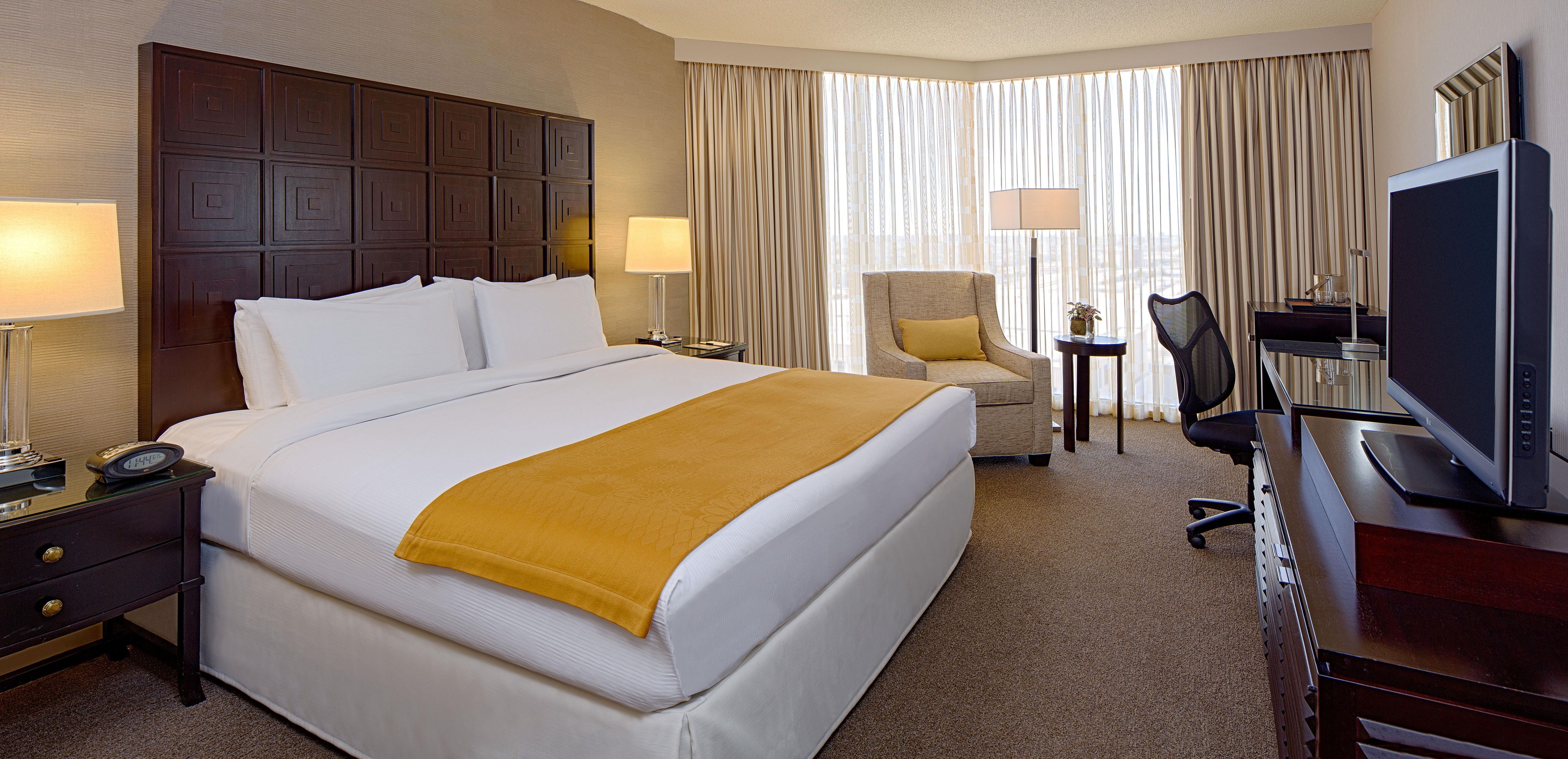 A hotel room with a large bed, a desk with a computer, a chair, and a television.