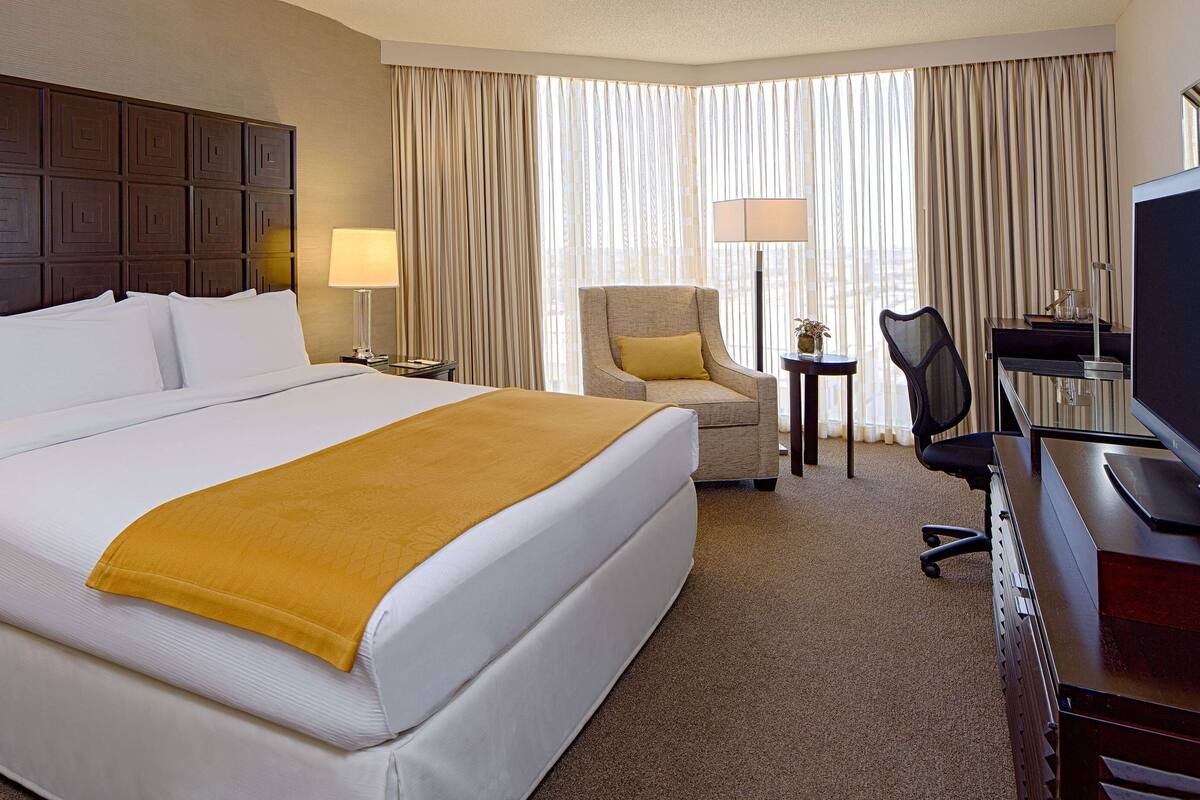 Une chambre d’hôtel avec un grand lit, un bureau avec une télévision, une chaise et deux lampes.