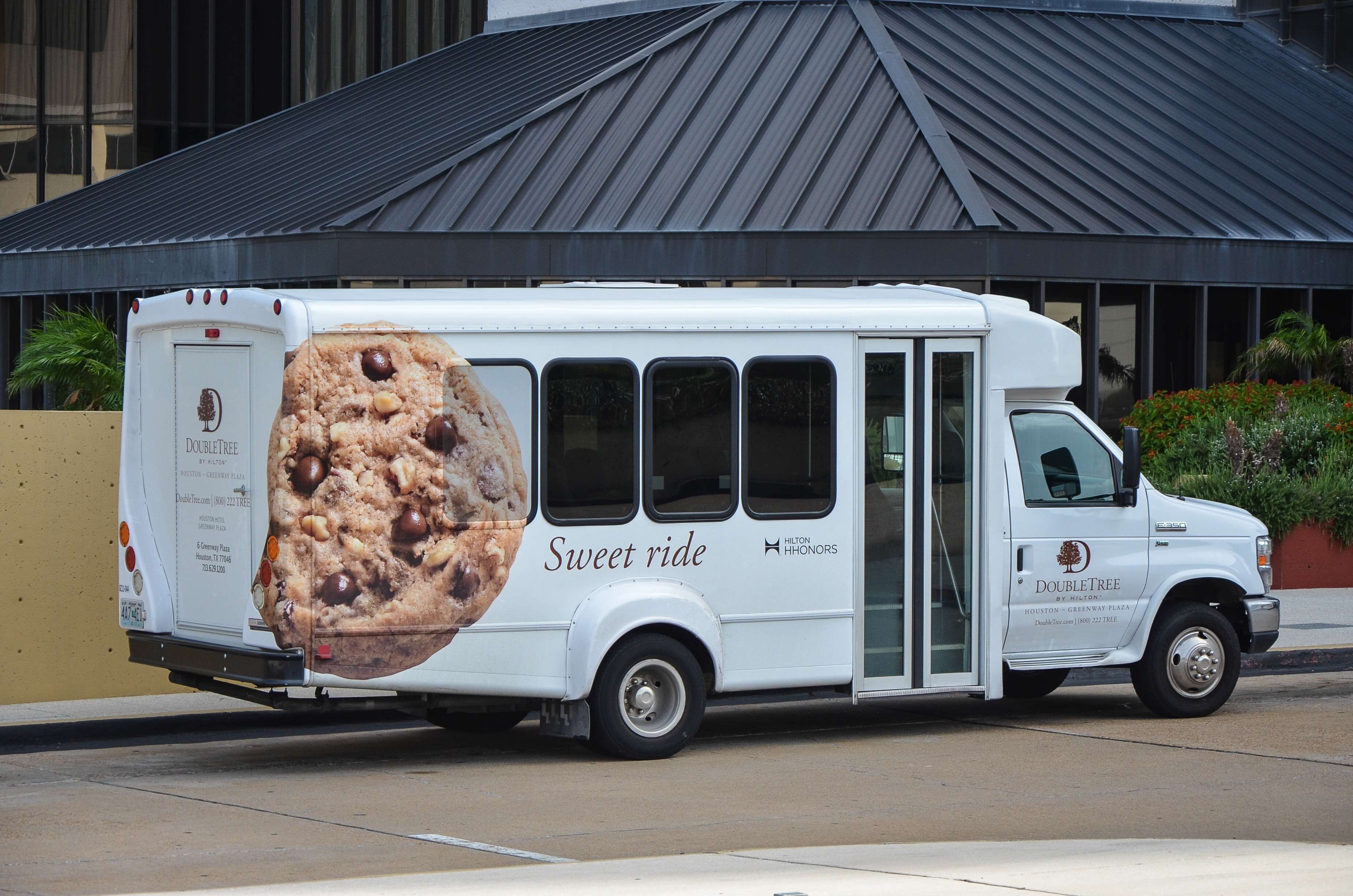 A white food truck with a large cookie advertisement on the side, parked in front of a building with a dark roof.