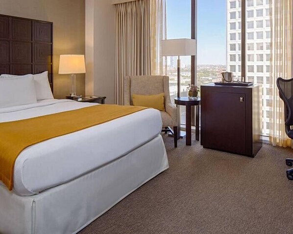 A hotel room with a large bed, a desk, a chair, and a view of the city. - DoubleTree by Hilton Hotel Houston - Greenway Plaza (Houston)