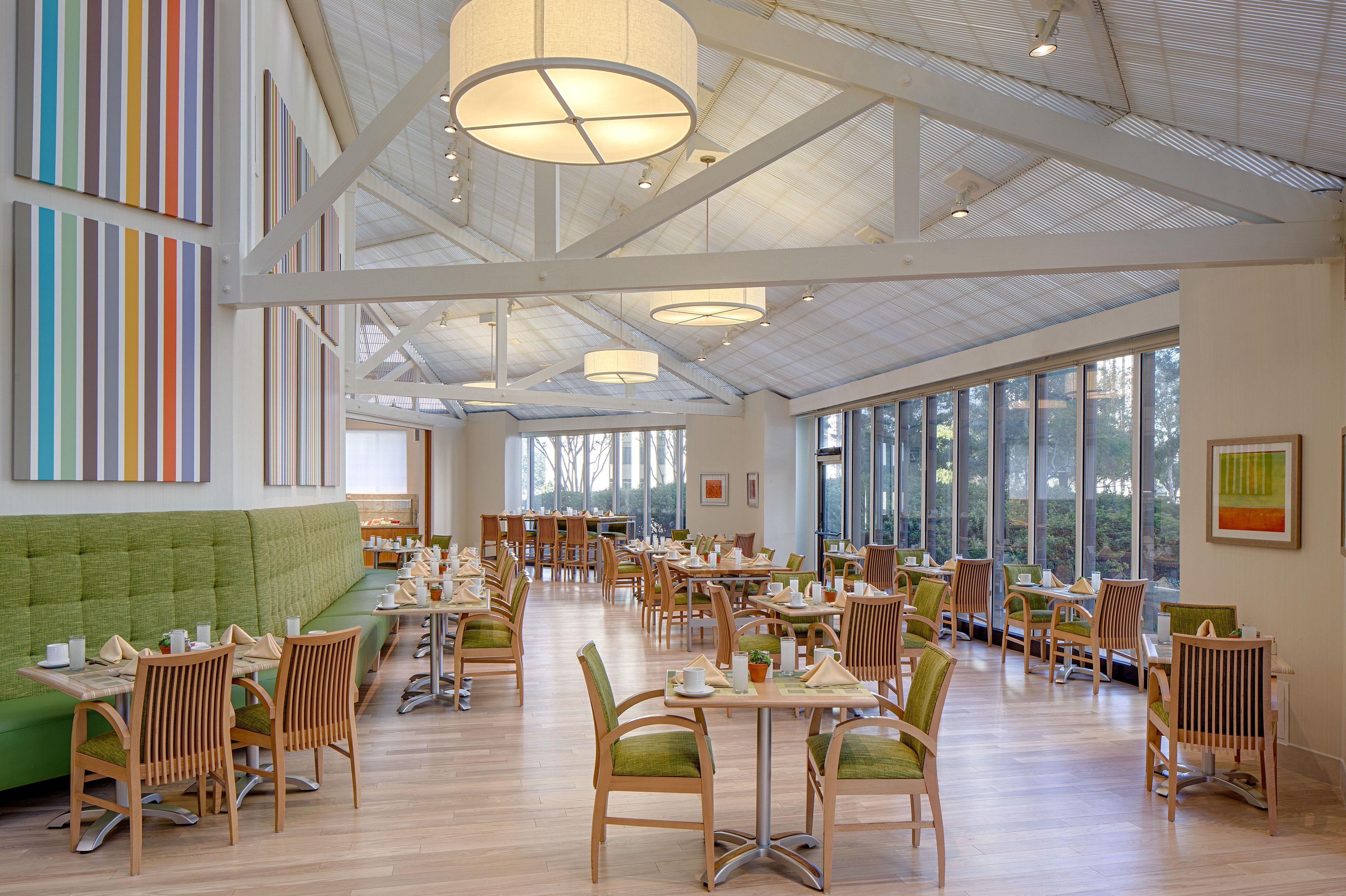 Un vaste espace dédié à la salle à manger, doté de hauts plafonds, de grandes fenêtres et d’un banc recouvert d’un tissu vert.