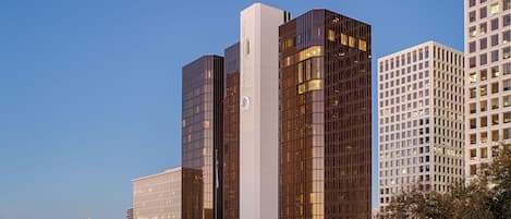 A modern hotel with a prominent glass facade, a well-maintained lawn, and a clear sky.