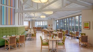 Un vaste espace dédié à la salle à manger, avec de hauts plafonds, de grandes fenêtres et un coin salon agrémenté de verdure.