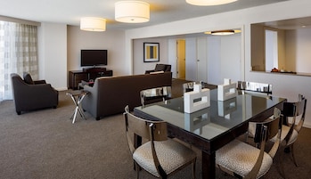 A hotel room with a dining area, a sofa, a television, and a mirror.