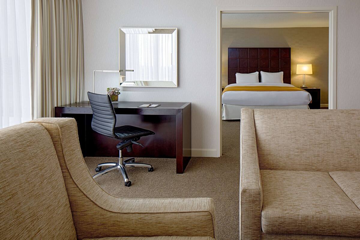 Une chambre d’hôtel équipée d’un bureau, d’un fauteuil de bureau, de deux canapés, d’un lit, d’une table de chevet et d’une lampe.