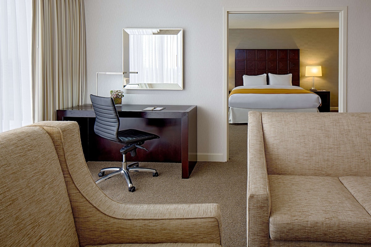 A hotel room with a desk, office chair, two sofas, a bed, a nightstand, and a lamp.