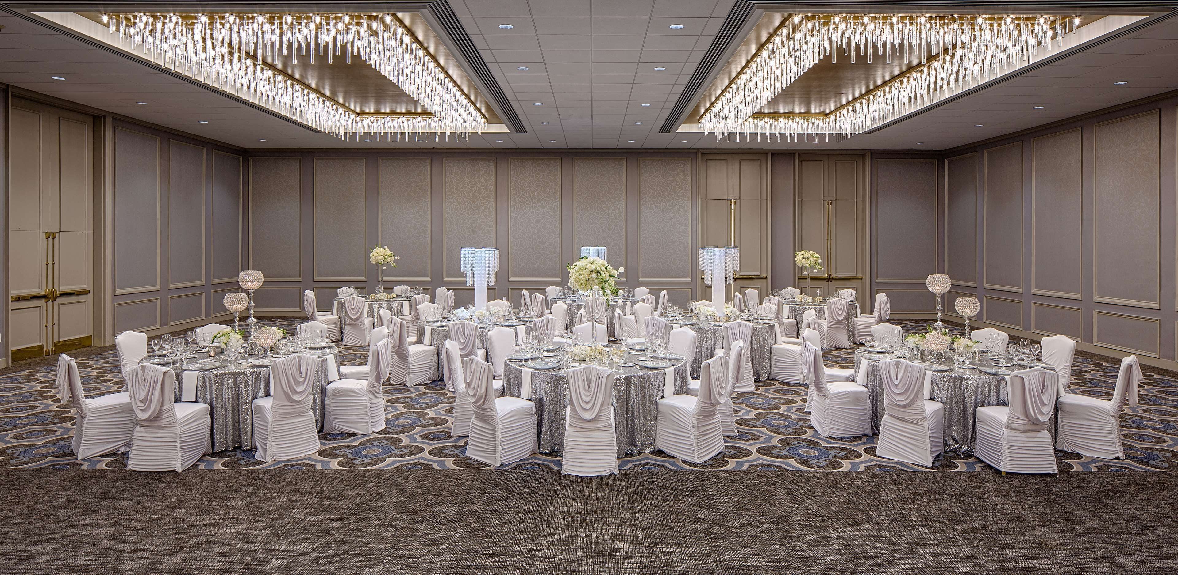 A large banquet hall with round tables, white chairs, and chandeliers.