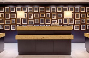 A reception desk with framed artwork on the wall behind it. - DoubleTree by Hilton Hotel Houston - Greenway Plaza (Houston)