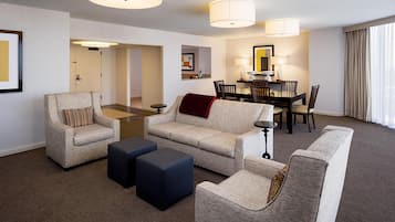 A hotel room with a living area, a dining table with chairs, a sofa, two ottomans, and a small side table.