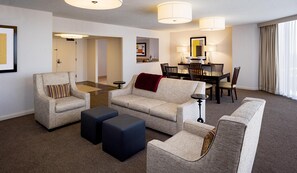 A hotel room with a living area, a dining table with chairs, a sofa, two ottomans, and a small side table. - DoubleTree by Hilton Hotel Houston - Greenway Plaza (Houston)