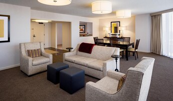 Habitación de hotel con sala de estar, una mesa de comedor con sillas, un sofá, dos otomanas y una pequeña mesita.