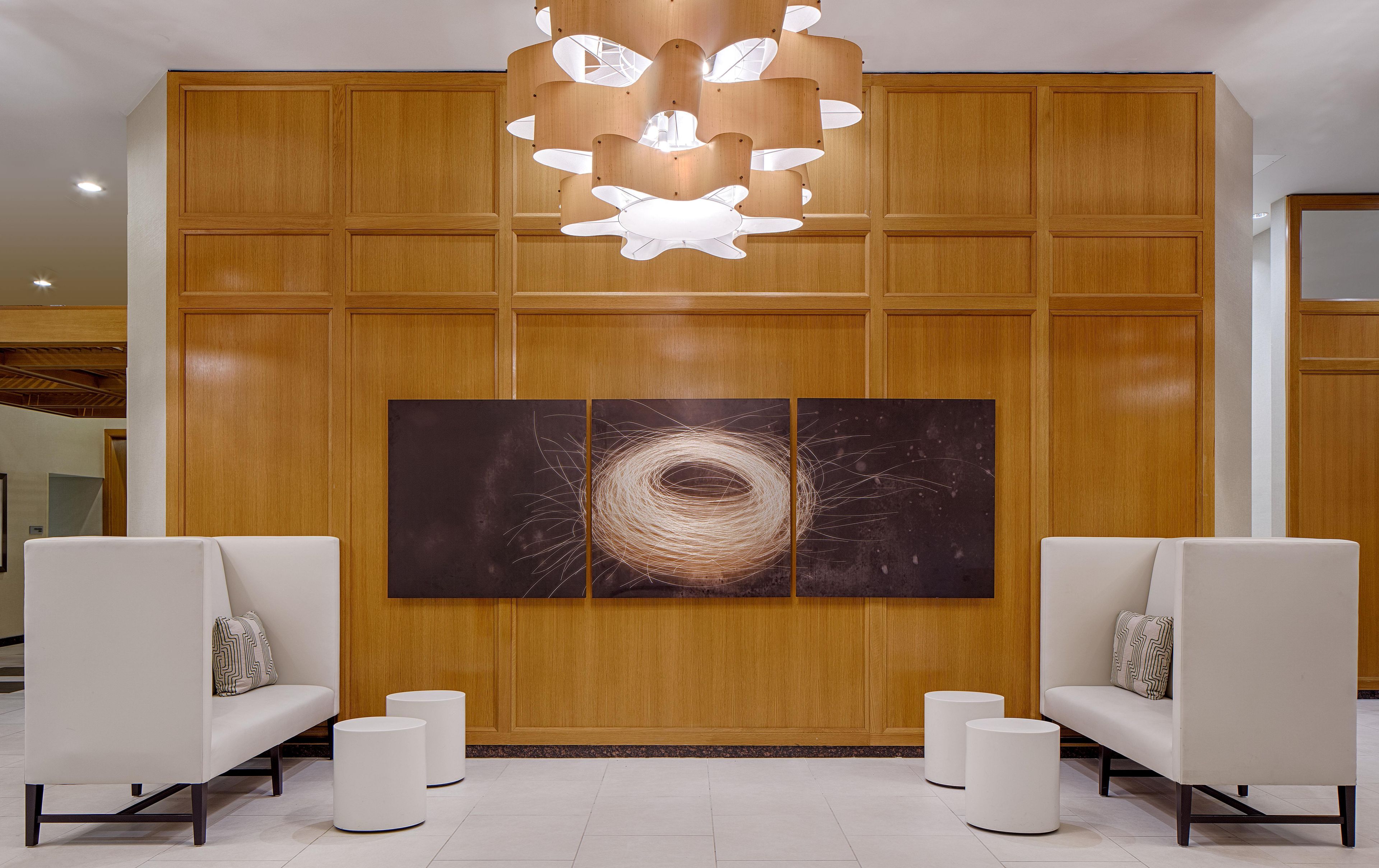 Un'area reception con parete rivestita in legno, un'ampia opera d'arte astratta, due divani bianchi con cuscini decorati e una moderna lampada a sospensione.