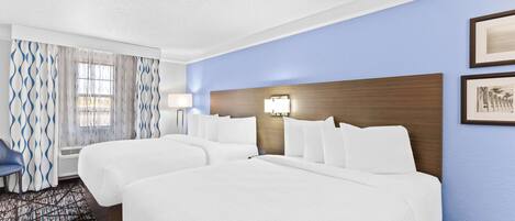 A hotel room with two beds, a desk, and a chair.
