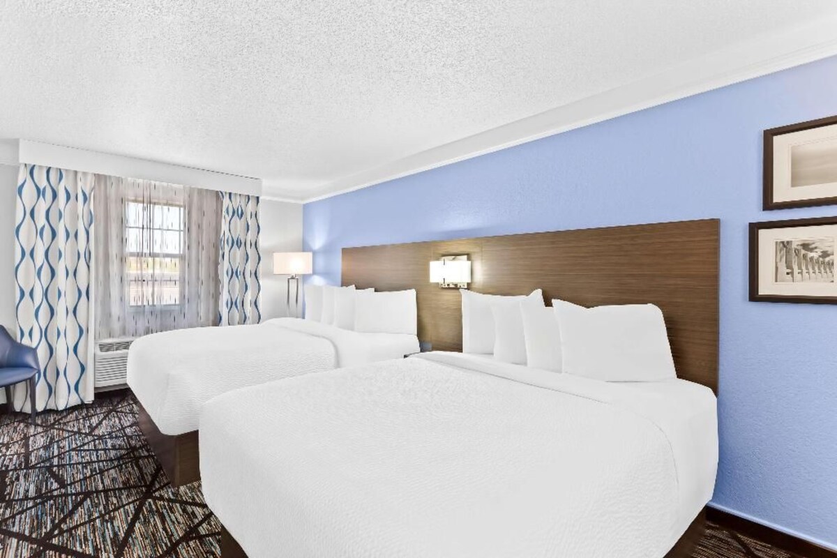 Une chambre d’hôtel avec deux lits, un bureau, une chaise et une fenêtre avec des rideaux.