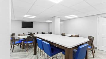 A conference room with a long table, blue chairs, and a flat-screen TV on the wall.