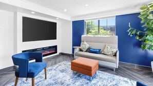 A modern living room with a flat-screen TV, a sofa with patterned cushions, a blue armchair, and a coffee table.