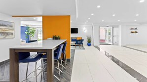 A modern hotel lobby with a long reception desk, blue bar stools, and a seating area with a sofa and chairs.