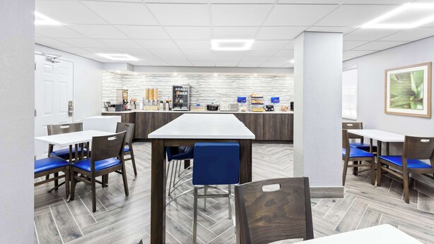 A modern dining area with a central island, blue chairs, and a white table.