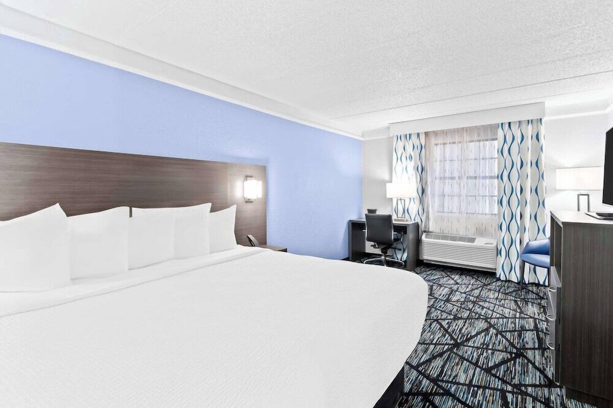 Une chambre d’hôtel avec un grand lit, un bureau avec une chaise, une lampe de bureau, une télévision et une fenêtre avec des rideaux.