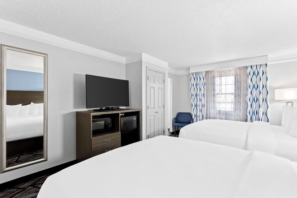 Habitación de hotel con una cama grande, televisión de pantalla plana, minibar, escritorio y una silla.