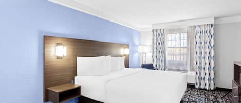A hotel room with a large bed, bedside lamps, a nightstand, a window with curtains, and a carpeted floor.