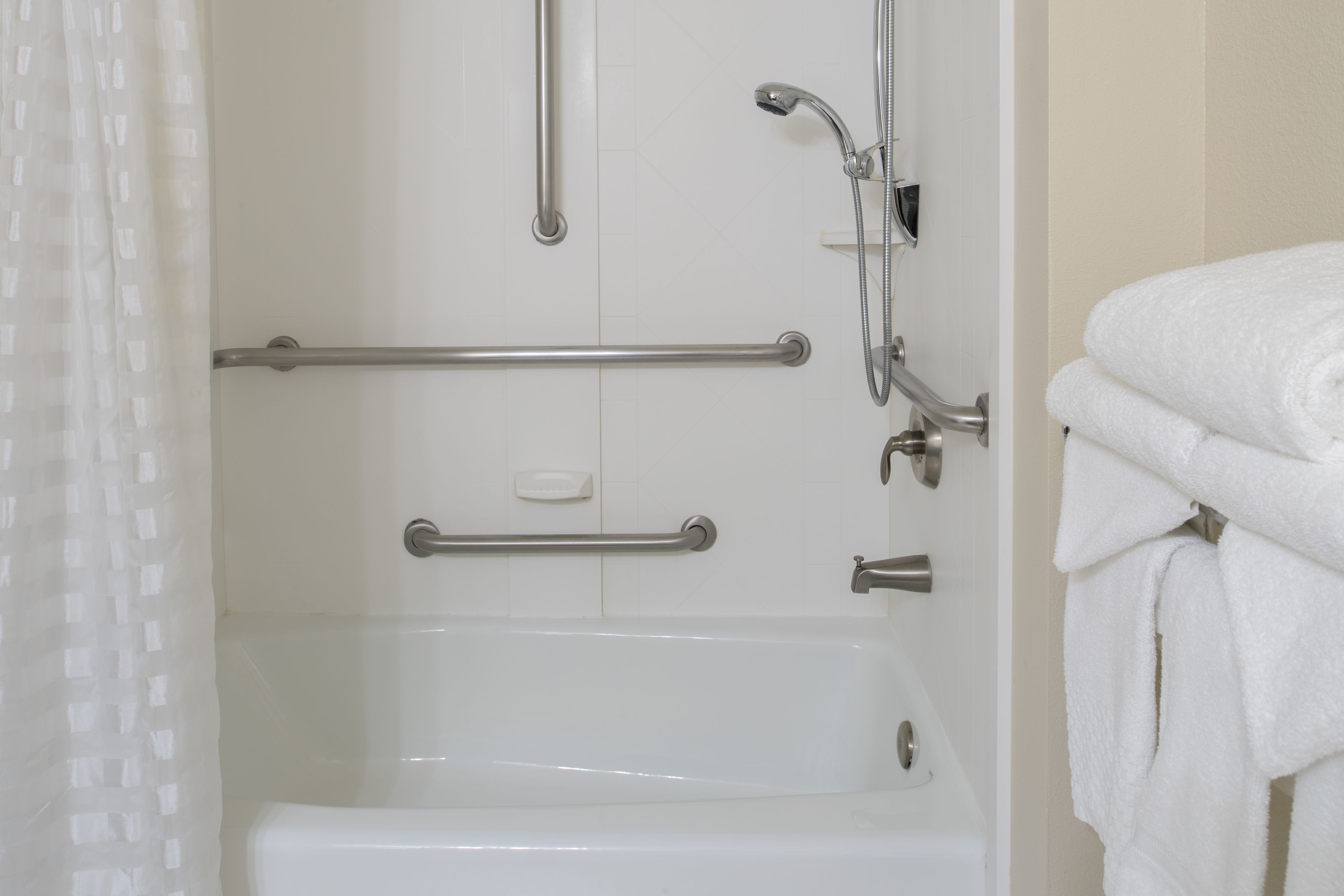 A bathroom with a bathtub, grab bars, a showerhead, and a towel rack.