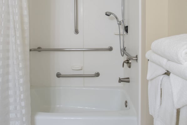 Un baño con bañera, barras de apoyo, cabezal de ducha y un perchero para toallas.