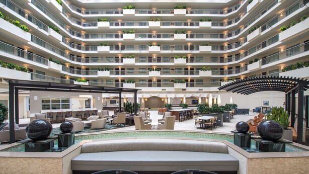 Een meerverdiepings hotelatrium met een centraal gelegen zwembad, zitgedeeltes en balkons met beplanting.
