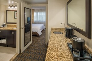A hotel bathroom with a sink, mirror, and a bed in the background. - Embassy Suites by Hilton Seattle Tacoma International Airport (Tukwila)