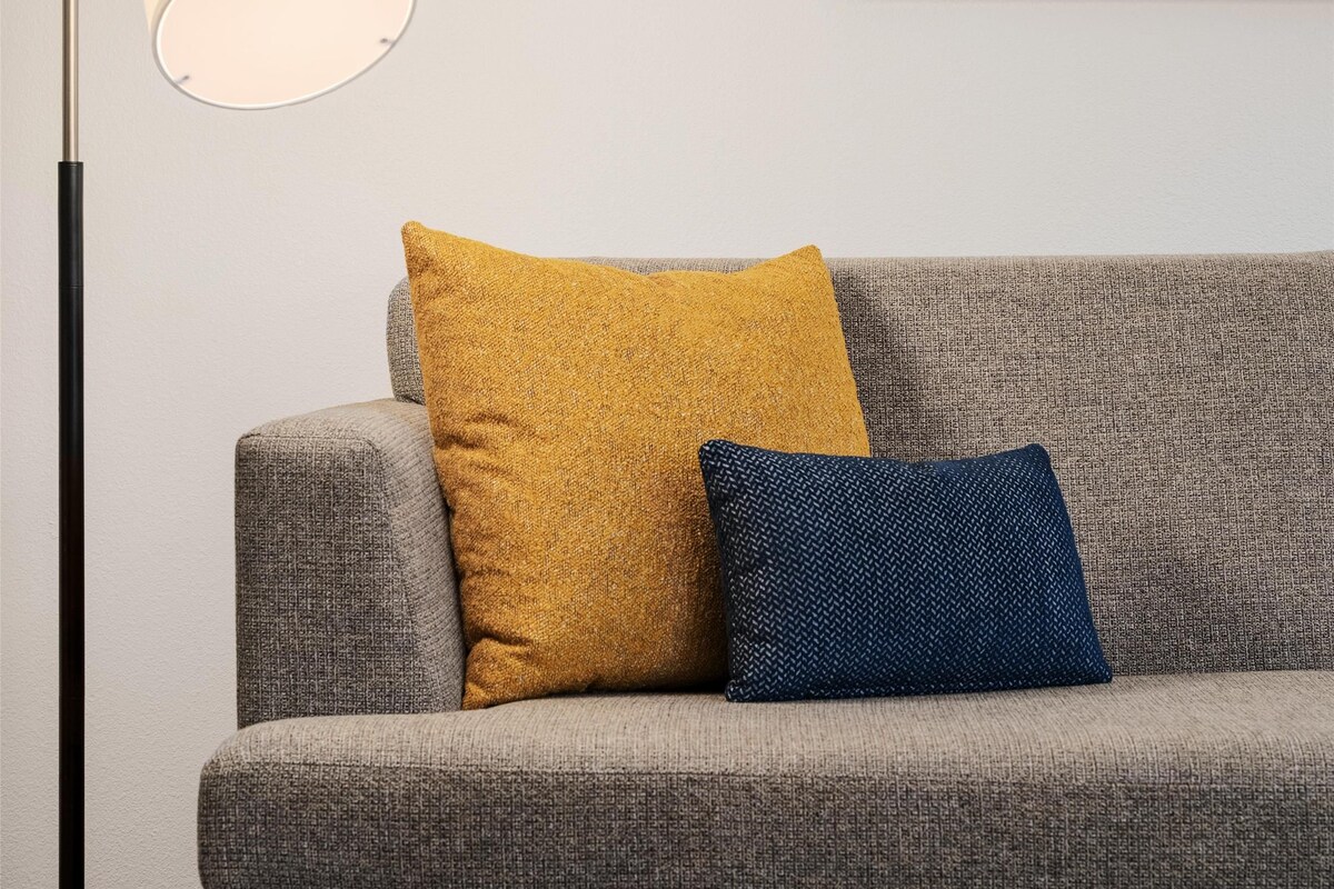 A grey sofa with two cushions, a floor lamp, and a framed abstract artwork on the wall.