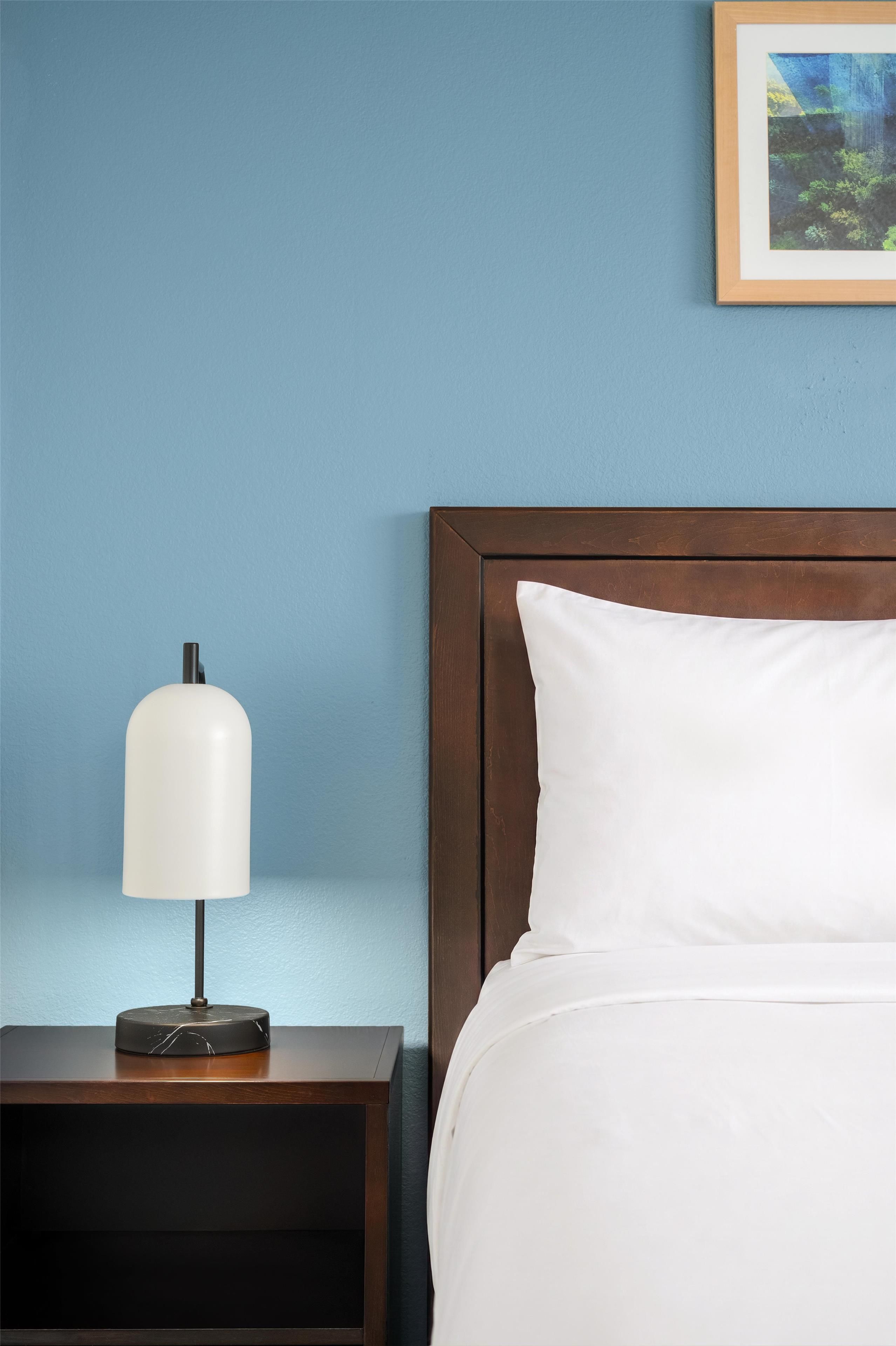 A neatly made bed with white linens, a wooden headboard, and a bedside table with a lamp.