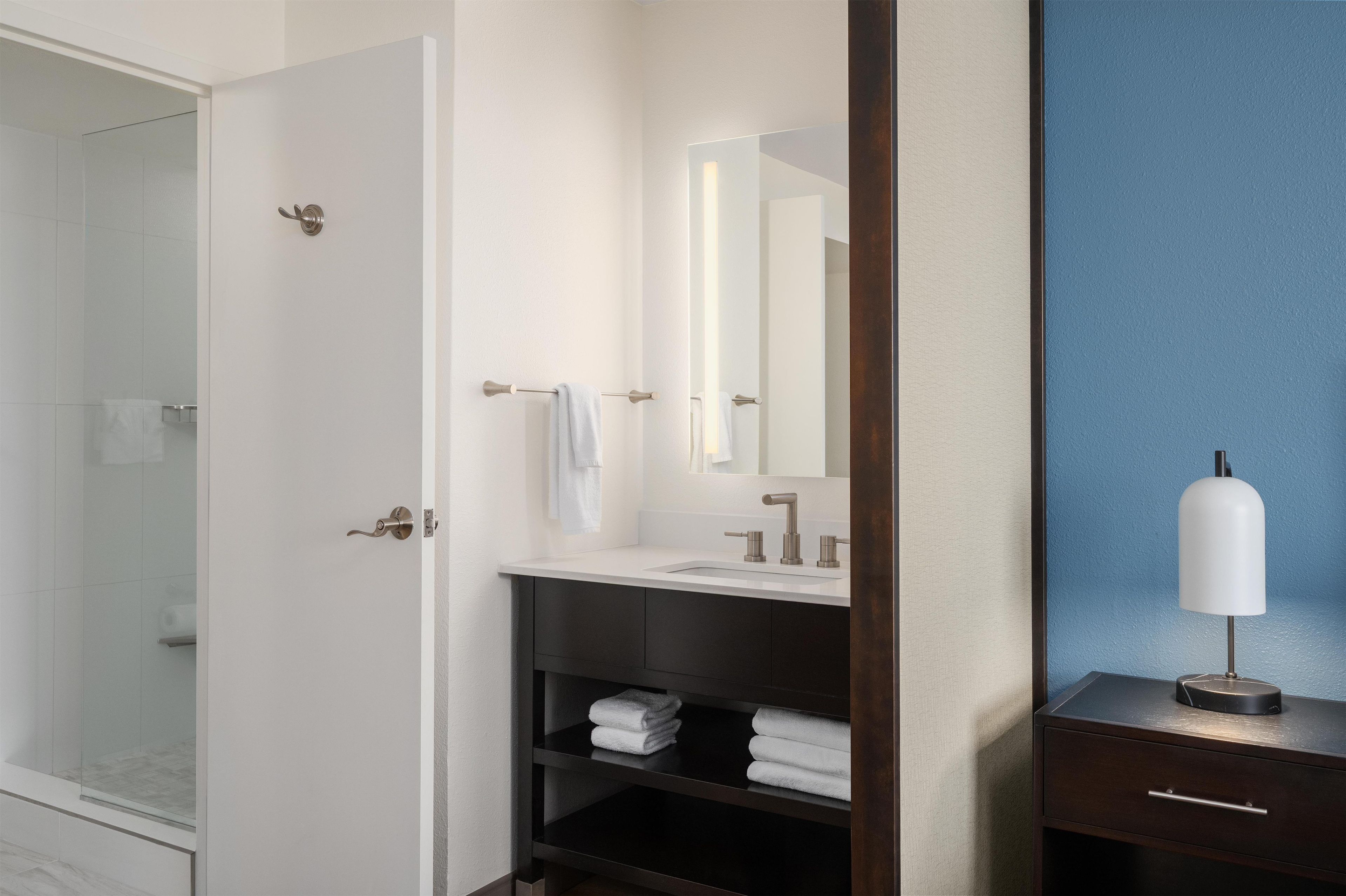 A modern bathroom with a glass shower enclosure, a white sink with a mirror, and a dark wooden vanity with a white lamp.