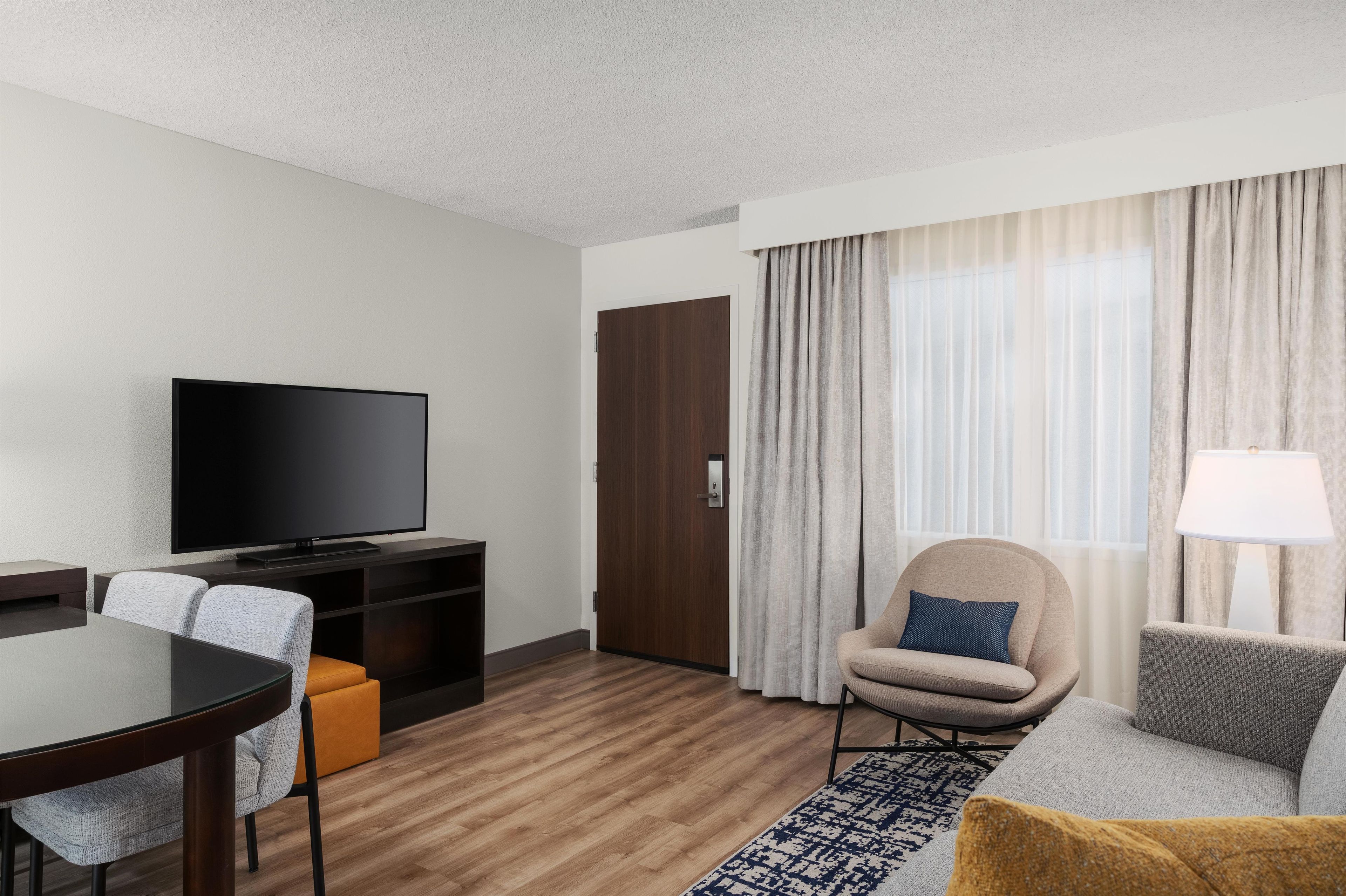 A hotel room with a flat-screen TV, a wooden coffee table, a sofa, a chair, and a lamp.
